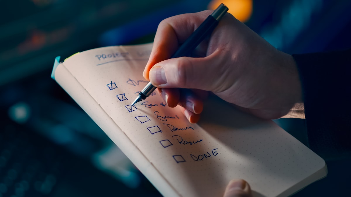 A hand writing a checklist in a notebook with a pen